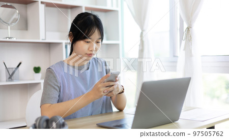 Asian woman having fun playing games on mobile phone, Play games on the sofa in the living room on weekends, Resting at home, Comfort zone, Touch screen mobile phone. 97505762