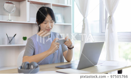 Asian woman having fun playing games on mobile phone, Play games on the sofa in the living room on weekends, Resting at home, Comfort zone, Touch screen mobile phone. Asian woman having fun playing games on mobile phone, Play games on the sofa in the living room on weekends, Resting at home, Comfort zone, Touch screen mobile phone. 97505766