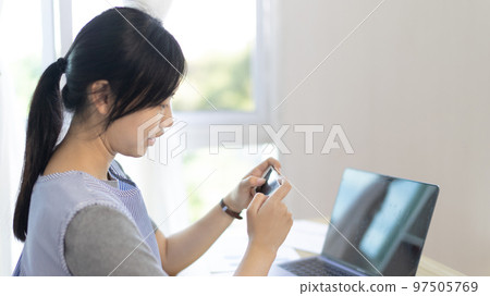 Asian woman having fun playing games on mobile phone, Play games on the sofa in the living room on weekends, Resting at home, Comfort zone, Touch screen mobile phone. Asian woman having fun playing games on mobile phone, Play games on the sofa in the living room on weekends, Resting at home, Comfort zone, Touch screen mobile phone. 97505769