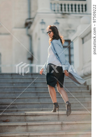 Woman walks in the city, lifestyle. Young beautiful woman in a loose light sweater, brown skirt and sneakers with a hat. Woman walks in the city, lifestyle. Young beautiful woman in a loose light sweater, brown skirt and sneakers with a hat. 97509222