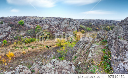 A large number of stone minerals covered with green vegetation lying above a small river in picturesque Ukraine and its beautiful nature 97510451