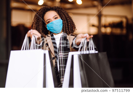 Young woman in protective medical mask with shopping bags 'near mall. Beautiful woman after shopping. 97511799