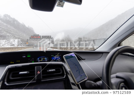 View from the driver's seat of a passenger car traveling on a highway where snow has begun to accumulate in winter View from the driver's seat of a passenger car traveling on a highway where snow has begun to accumulate in winter 97512589