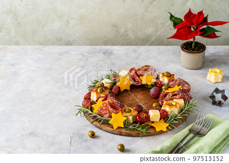 Christmas appetizers wreath on wooden board and grey background, star of Christmas plant or Poinsettia, napkin, forks. Copy space for text 97513152