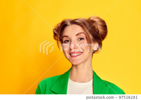Portrait of young cheerful girl in bright green jacket posing, smiling over yellow studio background. Positive 97516281