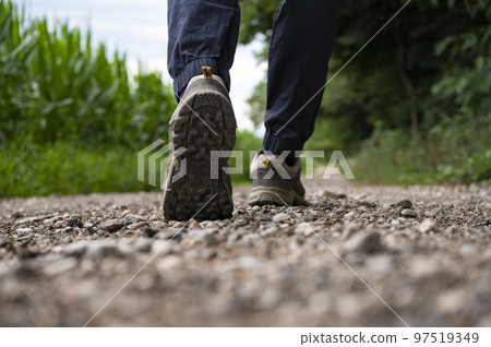 Low angle view of a sole of a man in hiking shoes walking on a gravel road 97519349
