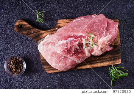 Raw pork ham, salt and rosemary on a cutting board on a dark background. Top view 97520920