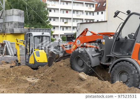 Small loader and excavator digger machine moving heap of earth and debris rubble at construction site. New building scaffold and engineering equipment rental. Construction site industrial background 97523531