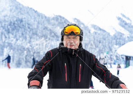 Active senior experienced mature old person in ski helmet, goggles and black suit stand against scenic panorama peak enjoy cold extreme sport activities. Man on mountains forest winter background Active senior experienced mature old person in ski helmet, goggles and black suit stand against scenic panorama peak enjoy cold extreme sport activities. Man on mountains forest winter background 97523532