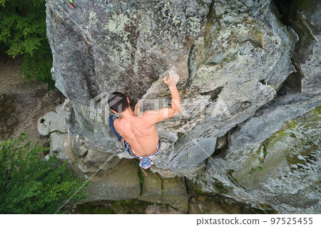 Young man climbing steep wall of rocky mountain. Male climber overcomes challenging route. Engaging in extreme sport concept. Young man climbing steep wall of rocky mountain. Male climber overcomes challenging route. Engaging in extreme sport concept. 97525455