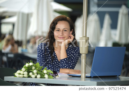 Young happy woman working remotely on laptop computer sitting at outdoor restaurant table. Doing business online concept Young happy woman working remotely on laptop computer sitting at outdoor restaurant table. Doing business online concept 97525474