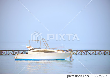 White motor boat floats in ocean water at long pier bridge under bright blue sky, view from sandy beach. Summer traveling concept White motor boat floats in ocean water at long pier bridge under bright blue sky, view from sandy beach. Summer traveling concept 97525664