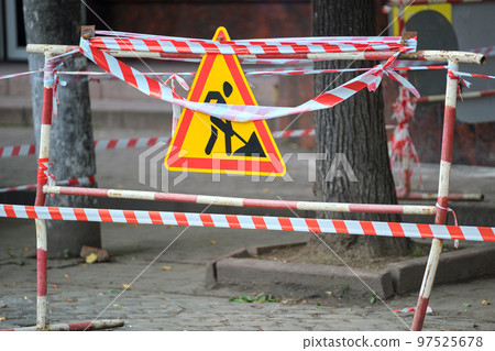 Warning roadworks sign and safety barrier on city street during maintenance repair work Warning roadworks sign and safety barrier on city street during maintenance repair work 97525678