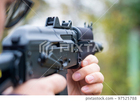 Man takes aim from an assault rifle side view close-up against the background of the forest Man takes aim from an assault rifle side view close-up against the background of the forest 97525788