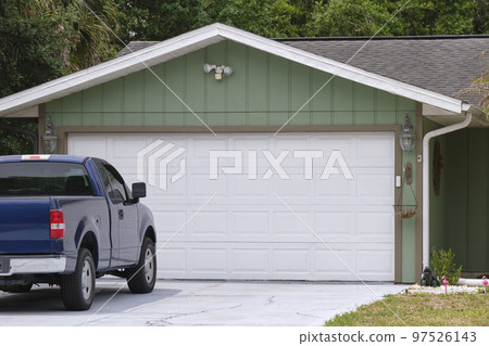 Vehicle parked in front of wide garage double door on paved driveway of typical contemporary american home 97526143