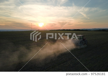 Tractor spraying fertilizers with insecticide herbicide chemicals on agricultural field at sunset 97526181