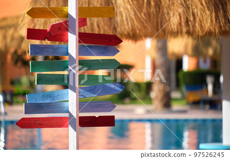 Summer recreation in tropical country. Colourful signboard pointing direction to outdoor pool, straw shadow parasols on sunny day 97526245