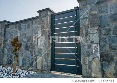Stone high fence with shut iron door in paved yard of modern style design property outdoor 97526251
