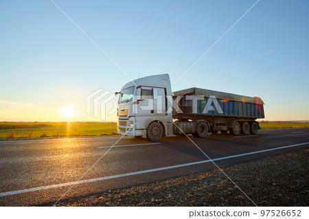 Semi-truck with tipping cargo trailer transporting sand from quarry driving on highway hauling goods in evening. Delivery transportation and logistics concept Semi-truck with tipping cargo trailer transporting sand from quarry driving on highway hauling goods in evening. Delivery transportation and logistics concept 97526652