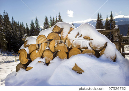 Neatly piled stack of chopped dry trunks wood covered with snow outdoors on bright cold winter sunny day, abstract background, Fire wood logs prepared for winter, ready for burning. 97526762