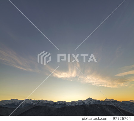 Mountain winter panorama landscape at dawn. Steep mountain peaks covered with snow and woody hills with spruce forest, raising bright sun on clear blue sky at sunrise copy space background. 97526764