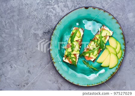 Tasty bruschetta with salmon, butter, avocado and arugula on a plate. Top view. Copy space 97527029