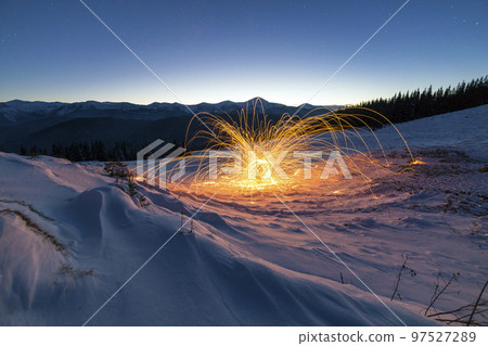 Light painting art. Spinning steel wool in abstract circle, firework showers of bright yellow glowing sparkles on winter snowy valley on mountain ridge and blue night starry sky copy space background. Light painting art. Spinning steel wool in abstract circle, firework showers of bright yellow glowing sparkles on winter snowy valley on mountain ridge and blue night starry sky copy space background. 97527289