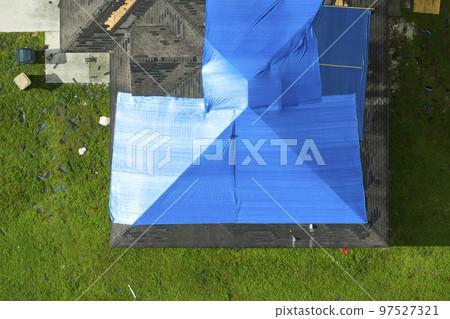 Hurricane Ian damaged house rooftop covered with protective plastic tarp against rain water leaking until replacement of asphalt shingles. Aftermath of natural disaster 97527321
