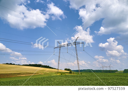 High voltage tower with electric power lines between green agricultural fields. Transfer of electricity concept 97527339