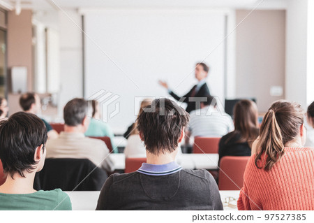 Speaker giving presentation in lecture hall at university. Participants listening to lecture and making notes. Copy space for brand on white screen. Speaker giving presentation in lecture hall at university. Participants listening to lecture and making notes. Copy space for brand on white screen. 97527385