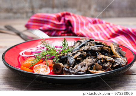 Fried mushrooms, onion and cherry tomatoes on a plate on a wooden table 97528069