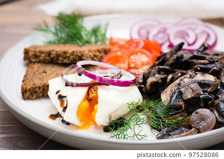 Appetizer of fried mushrooms, onions, tomatoes and poached eggs on a plate on a wooden table 97528086