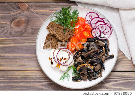 Appetizer of fried mushrooms, onions, tomatoes and poached eggs on a plate on a wooden table. Top view 97528090