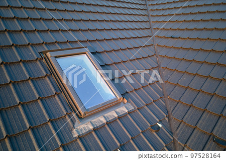 Closeup of attic window on house roof top covered with ceramic shingles. Tiled covering of building 97528164