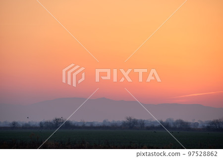 Beautiful evening panoramic landscape with bright setting sun over distant mountain peaks at sunset 97528862