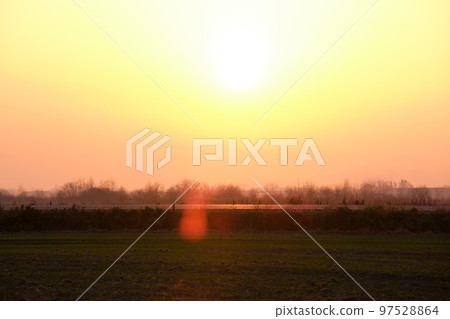 Beautiful evening panoramic landscape with bright setting sun over distant mountain peaks and asphalt road in front at sunset 97528864