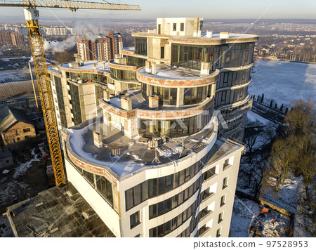 Aerial winter top view of modern developing city with tall apartment complex building under construction, parked cars, roofs and streets. Urban infrastructure, view from above. 97528953