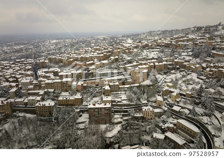 Aerial winter landscape of dense historic center of Thiers town in Puy-de-Dome department, Auvergne-Rhone-Alpes region in France. Rooftops of old buildings and narrow streets at snowfall 97528957