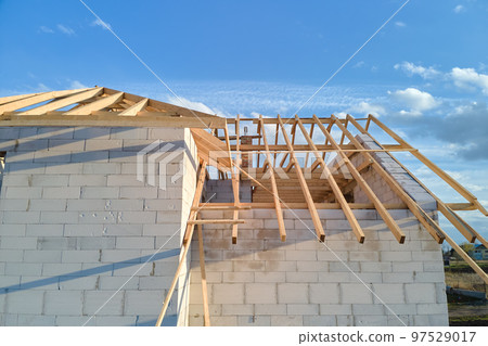Aerial view of unfinished frame of private house with aerated lightweight concrete walls and wooden roof frame under construction. Aerial view of unfinished frame of private house with aerated lightweight concrete walls and wooden roof frame under construction. 97529017