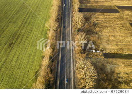Aerial view of straight road with moving cars, trees and green fields on sunny day. Drone photography. 97529084