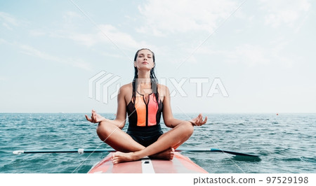 Woman sup yoga. Happy young sporty woman practising yoga pilates on paddle sup surfboard. Female stretching doing workout on sea water. Modern individual female outdoor summer sport activity. Woman sup yoga. Happy young sporty woman practising yoga pilates on paddle sup surfboard. Female stretching doing workout on sea water. Modern individual female outdoor summer sport activity. 97529198