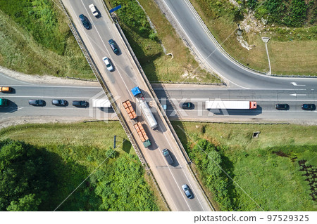 Aerial view of road intersection with fast moving heavy traffic on city streets. Uban transportation during rush hour with many cars and trucks Aerial view of road intersection with fast moving heavy traffic on city streets. Uban transportation during rush hour with many cars and trucks 97529325