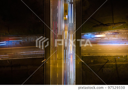 Aerial view of road intersection with fast moving heavy traffic at night. Top view of urban transportation. Rush hour with motion blurr car trail lights Aerial view of road intersection with fast moving heavy traffic at night. Top view of urban transportation. Rush hour with motion blurr car trail lights 97529330