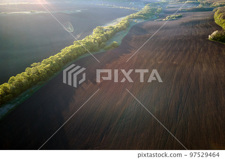Aerial view of plowed agricultural fields with cultivated fertile soil prepared for planting crops between green woods in spring 97529464