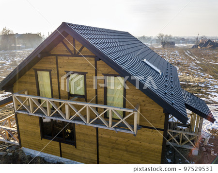 Aerial view of new wooden ecological traditional house cottage of natural lumber materials with steep shingle roof under construction on winter rural landscape background. Aerial view of new wooden ecological traditional house cottage of natural lumber materials with steep shingle roof under construction on winter rural landscape background. 97529531