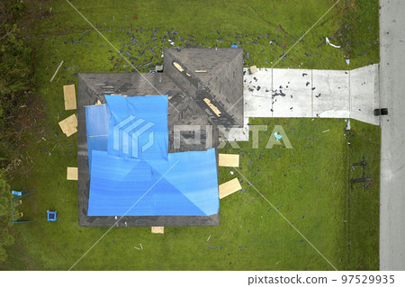 Aerial view of damaged in hurricane Ian house roof covered with blue protective tarp against rain water leaking until replacement of asphalt shingles 97529935