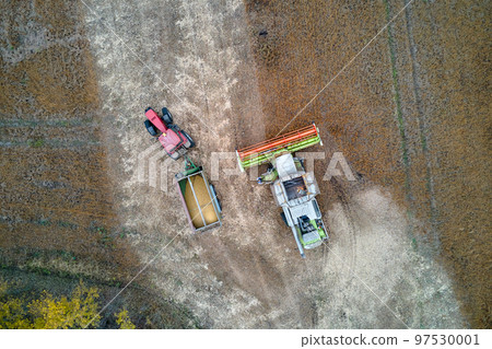 Aerial view of combine harvester unloading grain in cargo trailer working during harvesting season on large ripe wheat field. Agriculture and transportation of raw farm products concept Aerial view of combine harvester unloading grain in cargo trailer working during harvesting season on large ripe wheat field. Agriculture and transportation of raw farm products concept 97530001