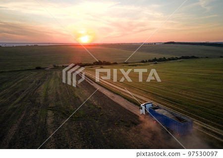 Aerial view of cargo truck driving on dirt road between agricultural wheat fields making lot of dust. Transportation of grain after being harvested by combine harvester during harvesting season Aerial view of cargo truck driving on dirt road between agricultural wheat fields making lot of dust. Transportation of grain after being harvested by combine harvester during harvesting season 97530097