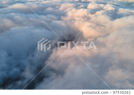 Aerial view from high altitude of distant city covered with puffy cumulus clouds forming before rainstorm in evening. Airplane point of view of cloudy landscape 97530261