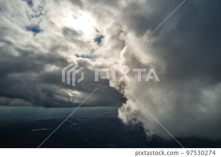 Aerial view from airplane window at high altitude of distant city covered with puffy cumulus clouds forming before rainstorm 97530274